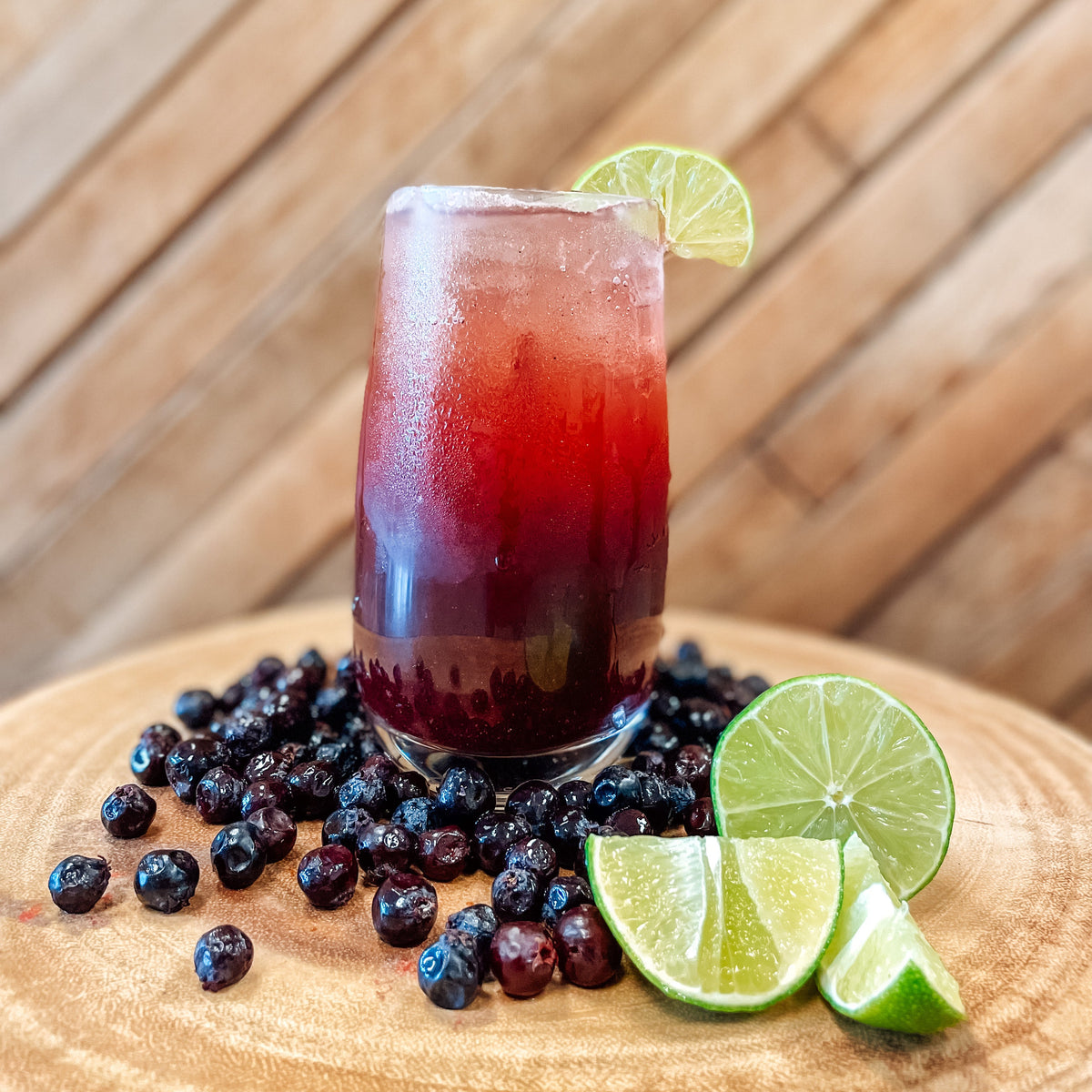 Fruity drink with ice and lime garnish on a wooden surface with berries